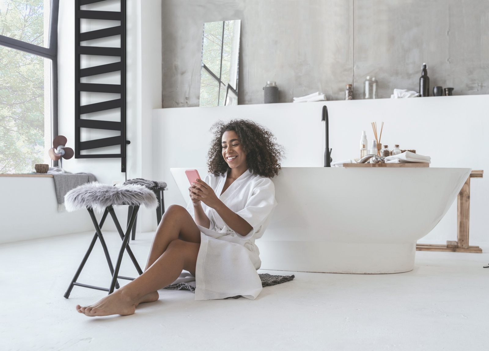 Smiling woman sitting in the bathroom on the floor with a smartphone in her hands